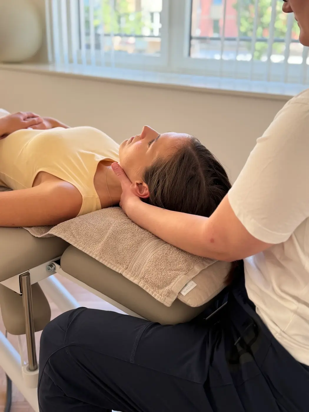 Physiotherapeutin von Eden Physiotherapie München behandelt den Nacken einer entspannt liegenden Patientin im Behandlungsraum